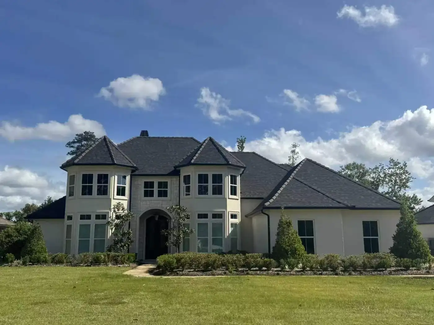 Large two-story stucco and stone estate with bay windows and landscaped lawn under a blue sky