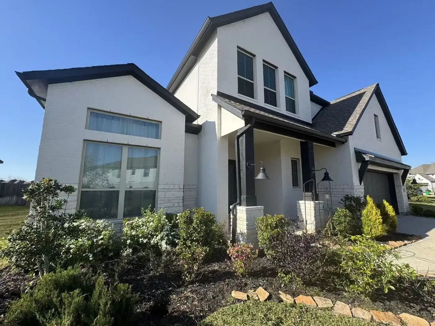 Modern white brick farmhouse with black trim, covered front porch and flowering landscaping