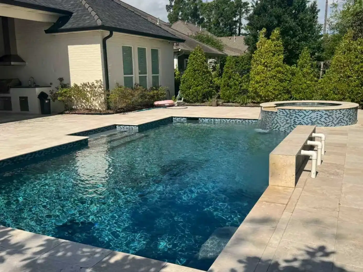 Custom swimming pool with circular spa, waterfall feature and stone patio surrounded by lush greenery