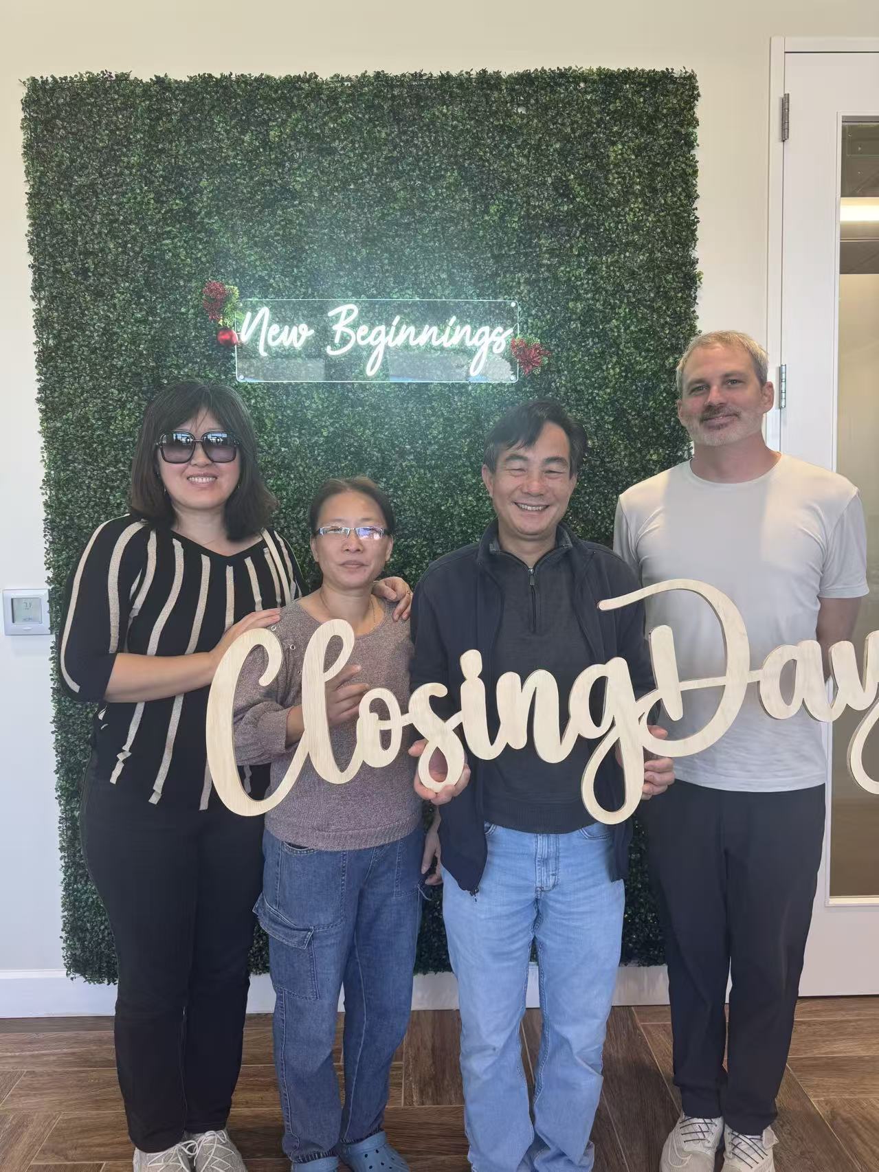 Clients holding a Closing Day sign in front of the New Beginnings green wall